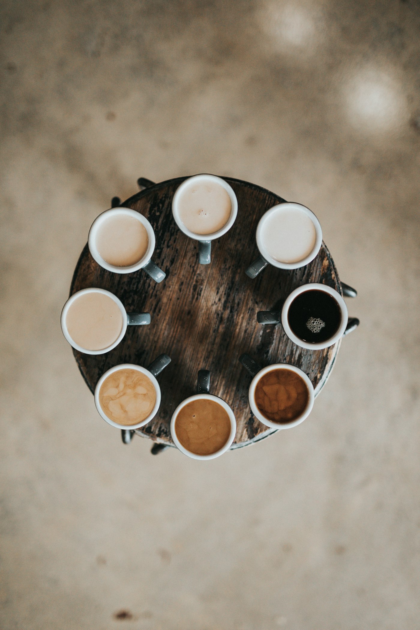 Acht koppen koffie in een cirkel op een houten kruk