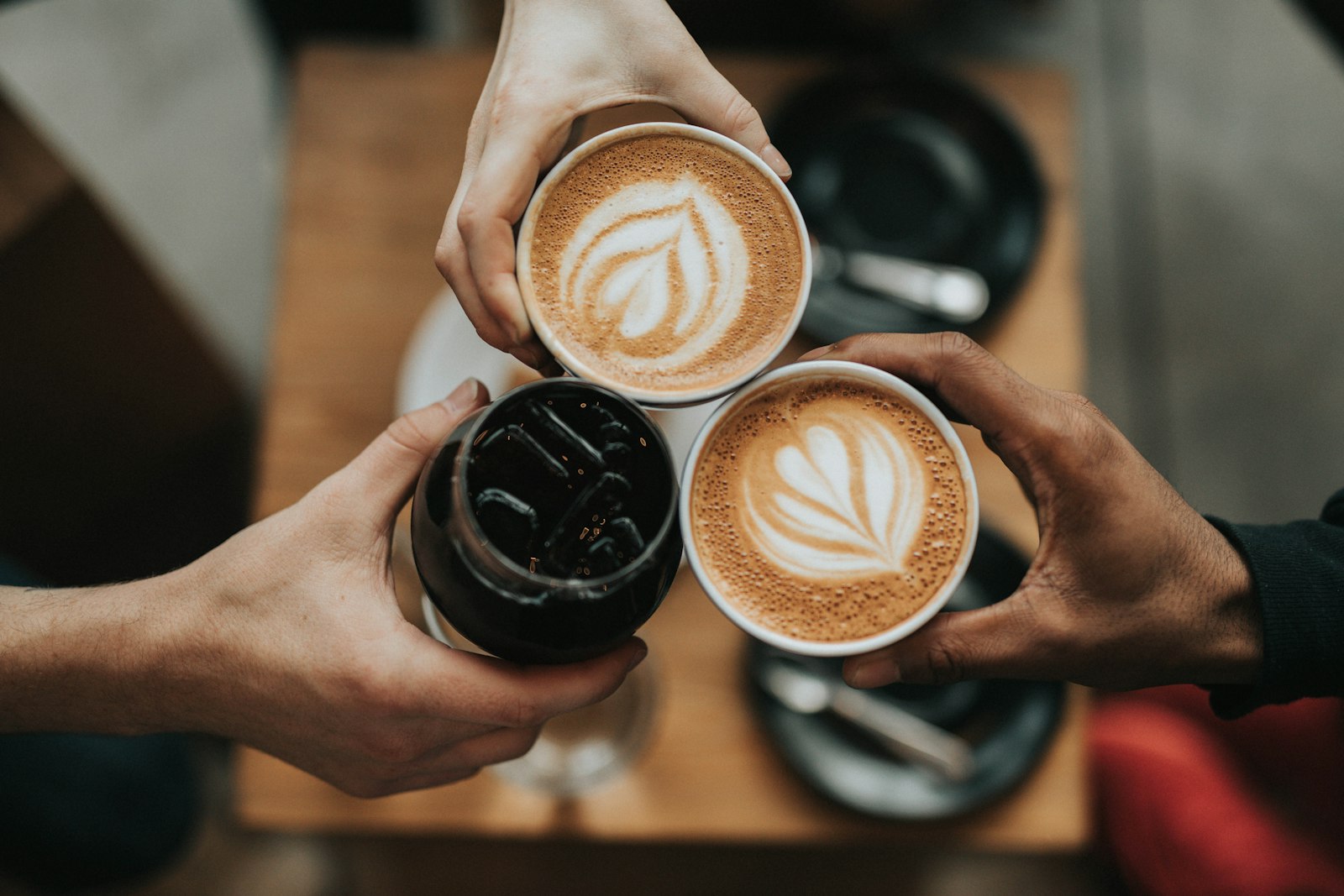 Drie mensen klinken met koffiekoppen boven een houten tafel